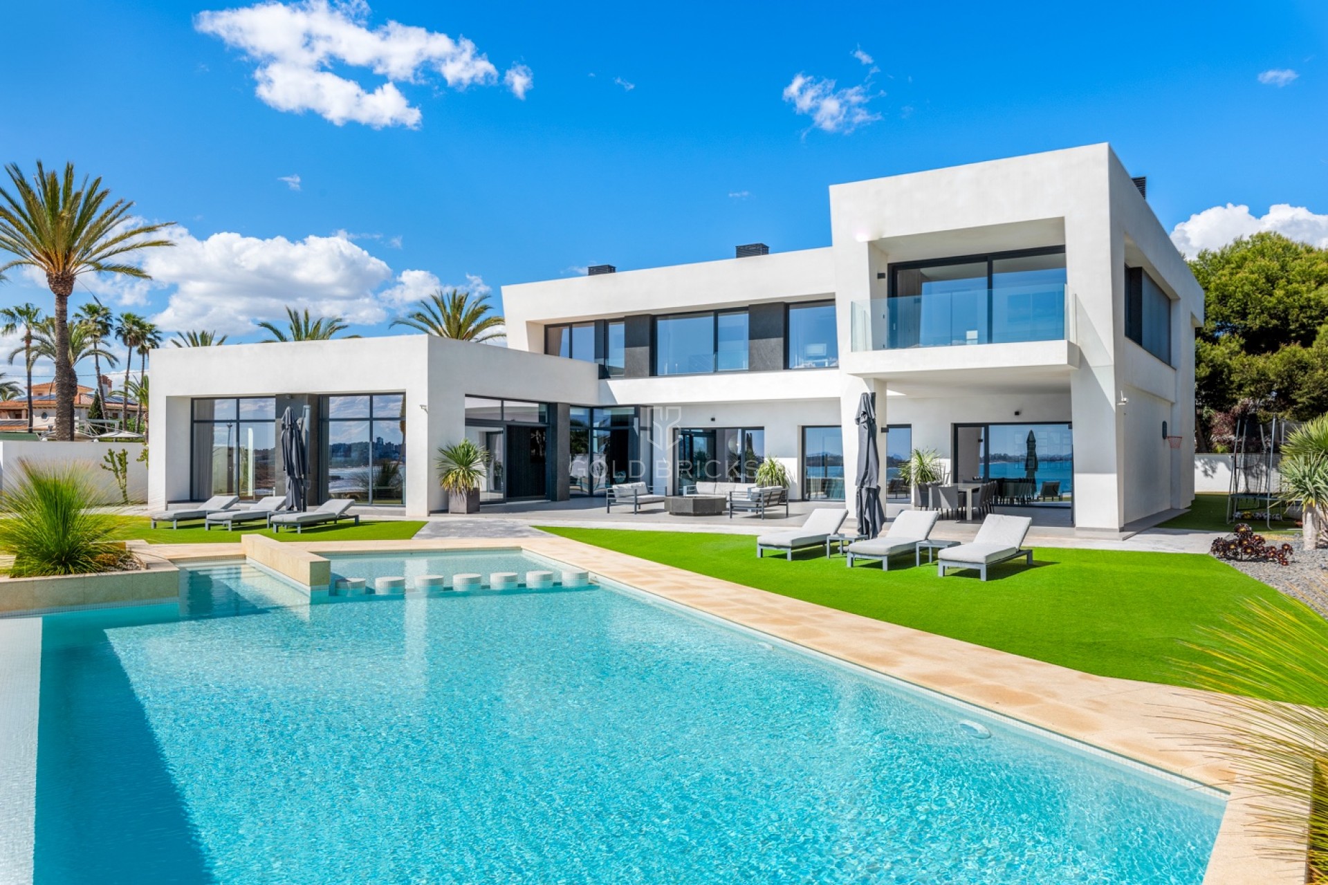 Fachada de la villa de Cabo Roig con piscina y palmeras a mediodía